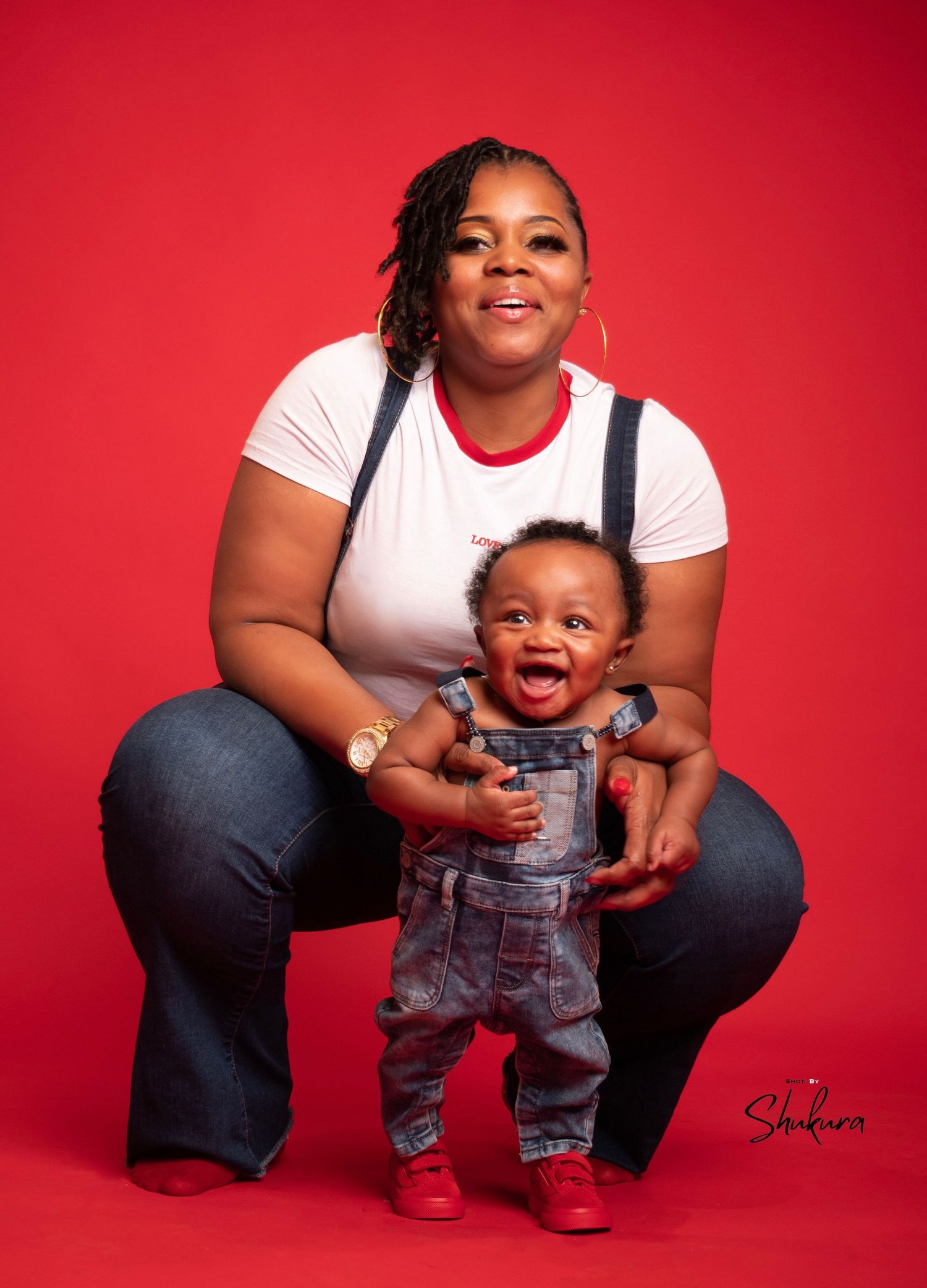 Parent and child pose together during indoor portrait session with bright red background.