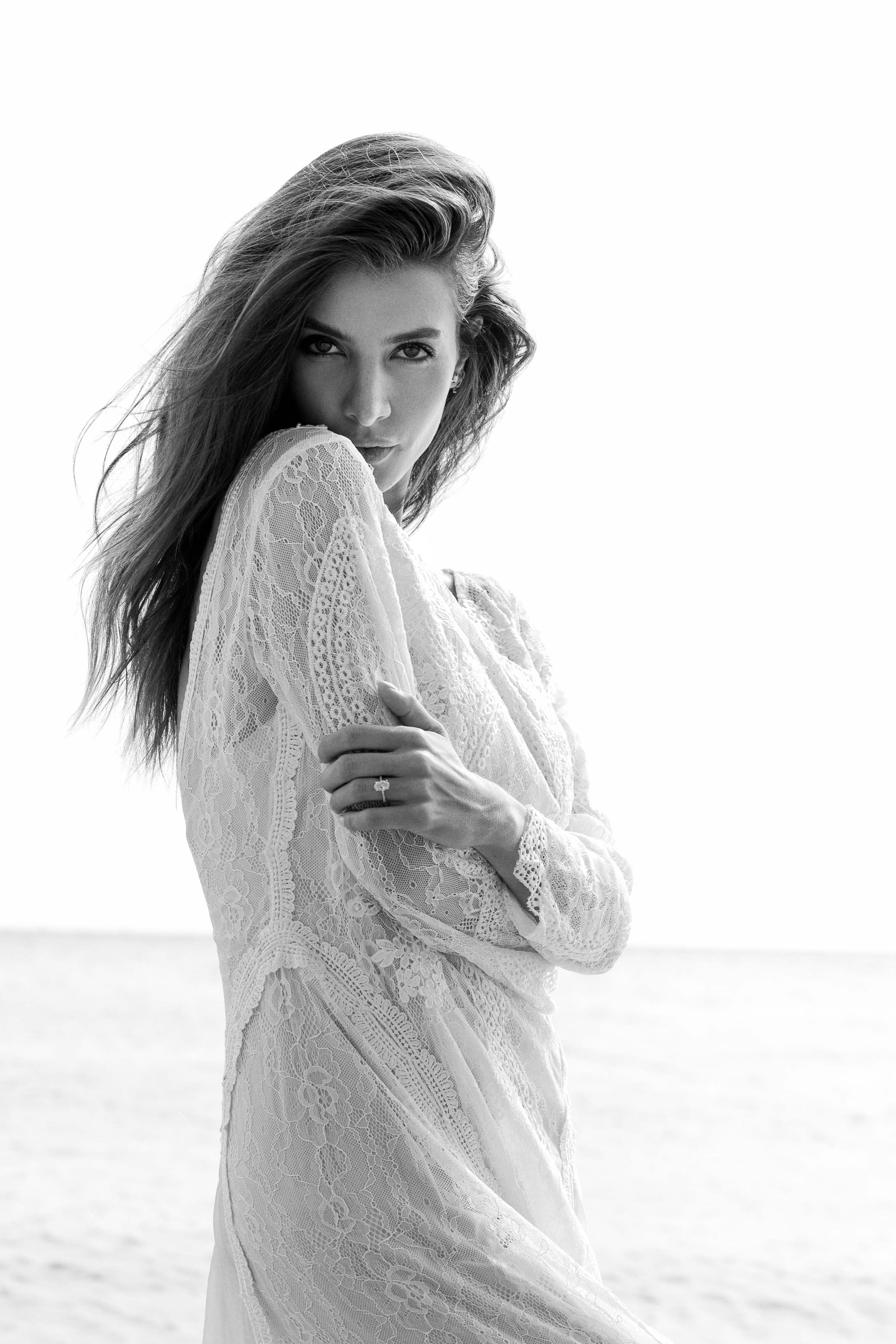 Black and white artistic portrait of woman in lace dress with windswept hair against bright background.
