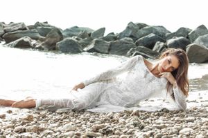 A series of dreamy bridal photos showing a person in a white dress lying gracefully on a rocky beach near the ocean.
