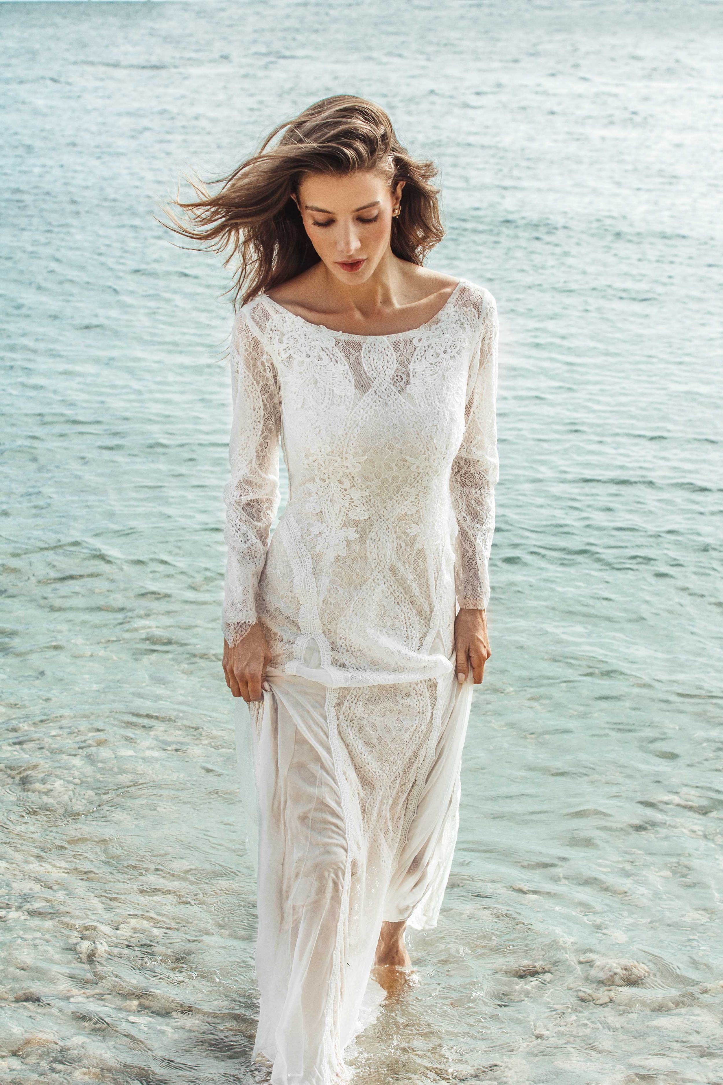 A bohemian bridal gown with delicate lace detailing and long sleeves worn on a serene turquoise beach.