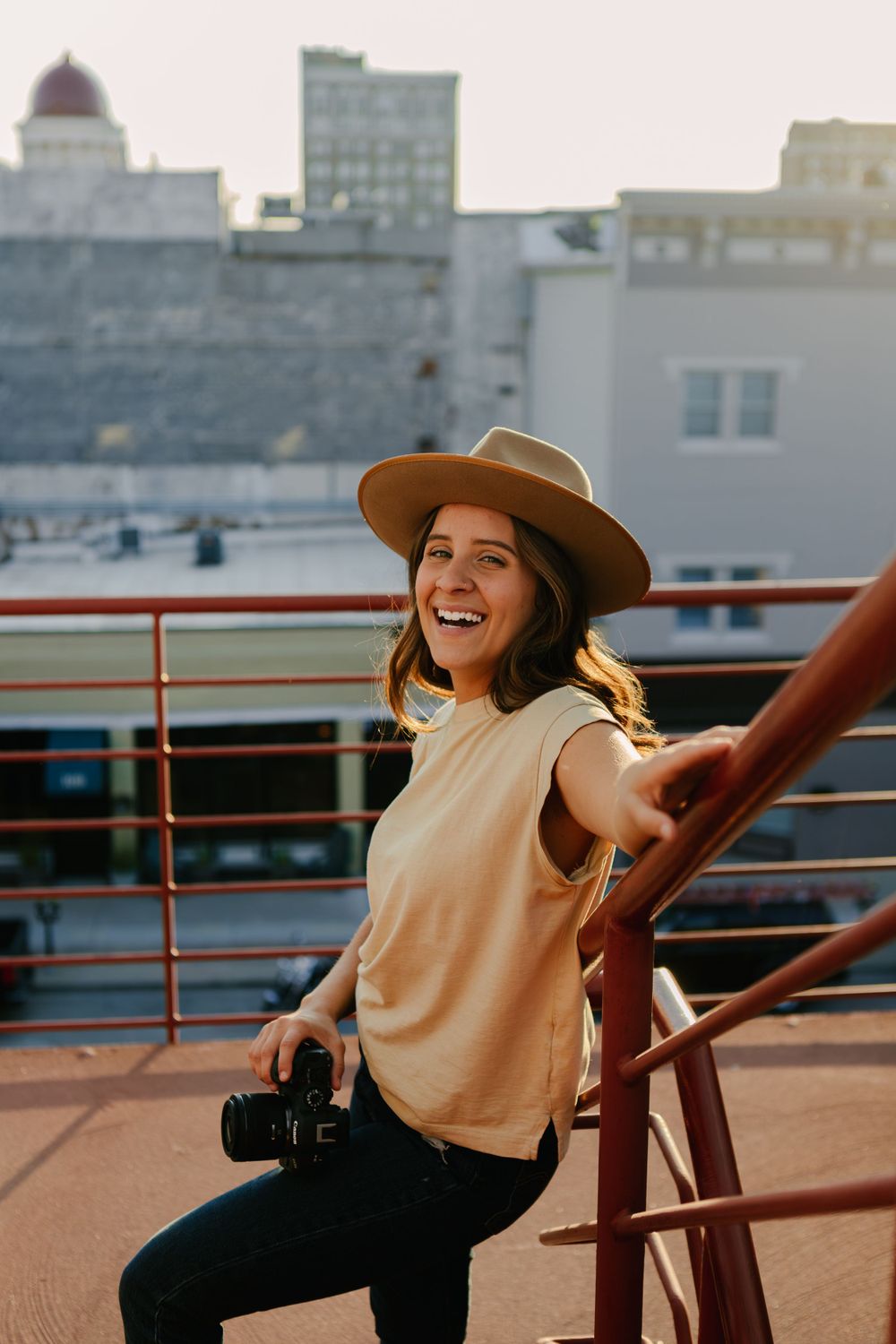 Photographer with camera sits on rooftop railing at golden hour in urban setting.