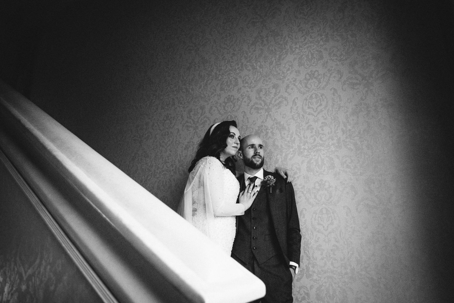 A dramatic black and white wedding photo of a couple on stairs against a textured wall.