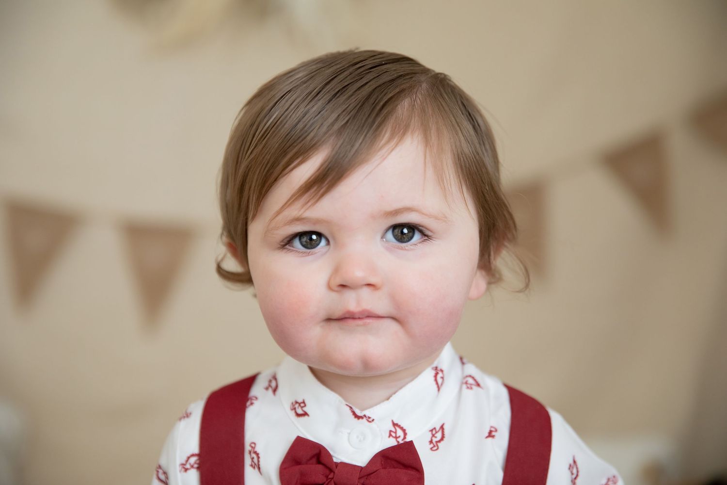 A toddler in red suspenders and bow tie smiling at the camera.