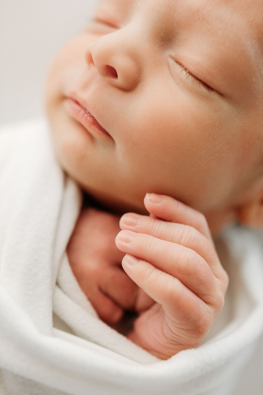 Close-up of sleeping infant's face with tiny hand resting near chin.