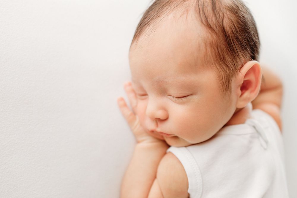 Peaceful sleeping infant in white clothing against light background.
