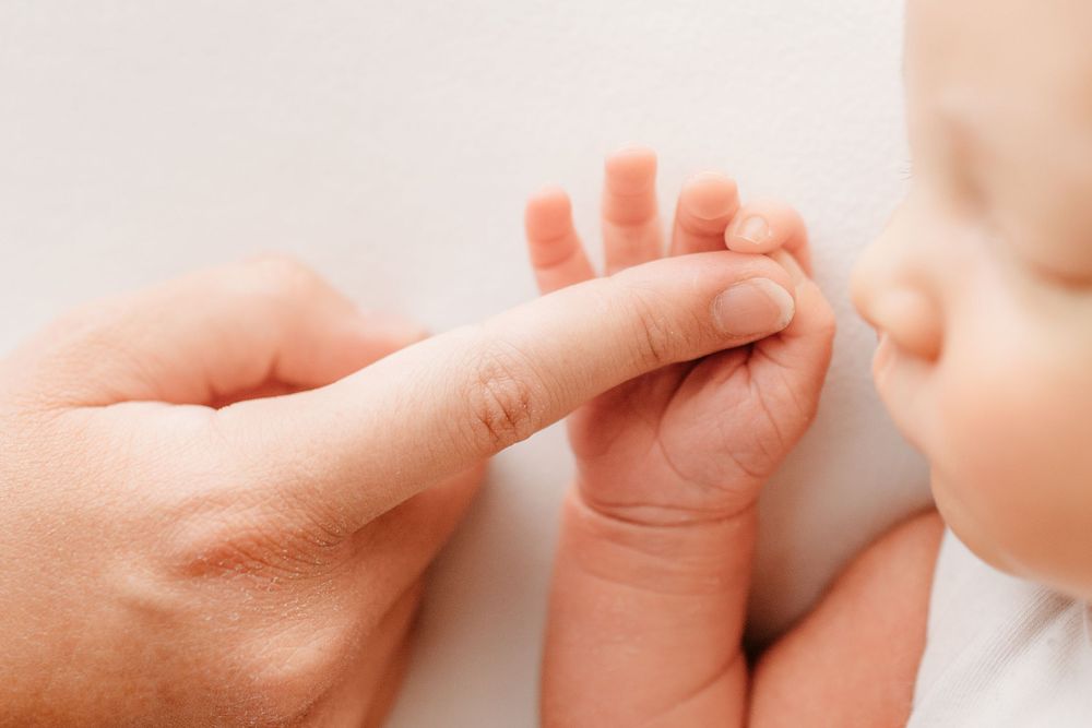 Close-up of tiny baby hand grasping adult finger.
