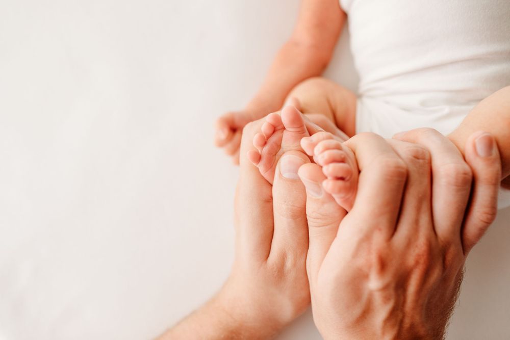 Adult hands gently holding tiny newborn feet against white background.