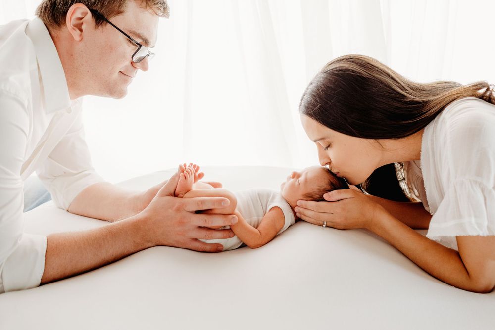Parents lovingly admiring their newborn baby on white surface.
