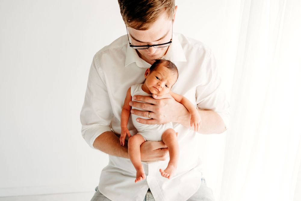 A tender moment captured in white as a parent cradles a newborn baby against a minimalist background.