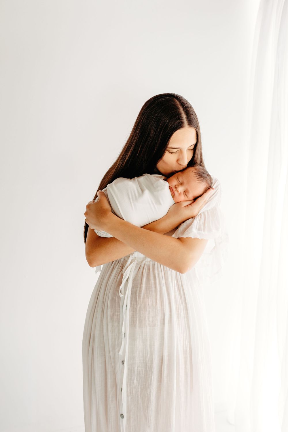 A gentle embrace between parent and newborn baby against a white backdrop.