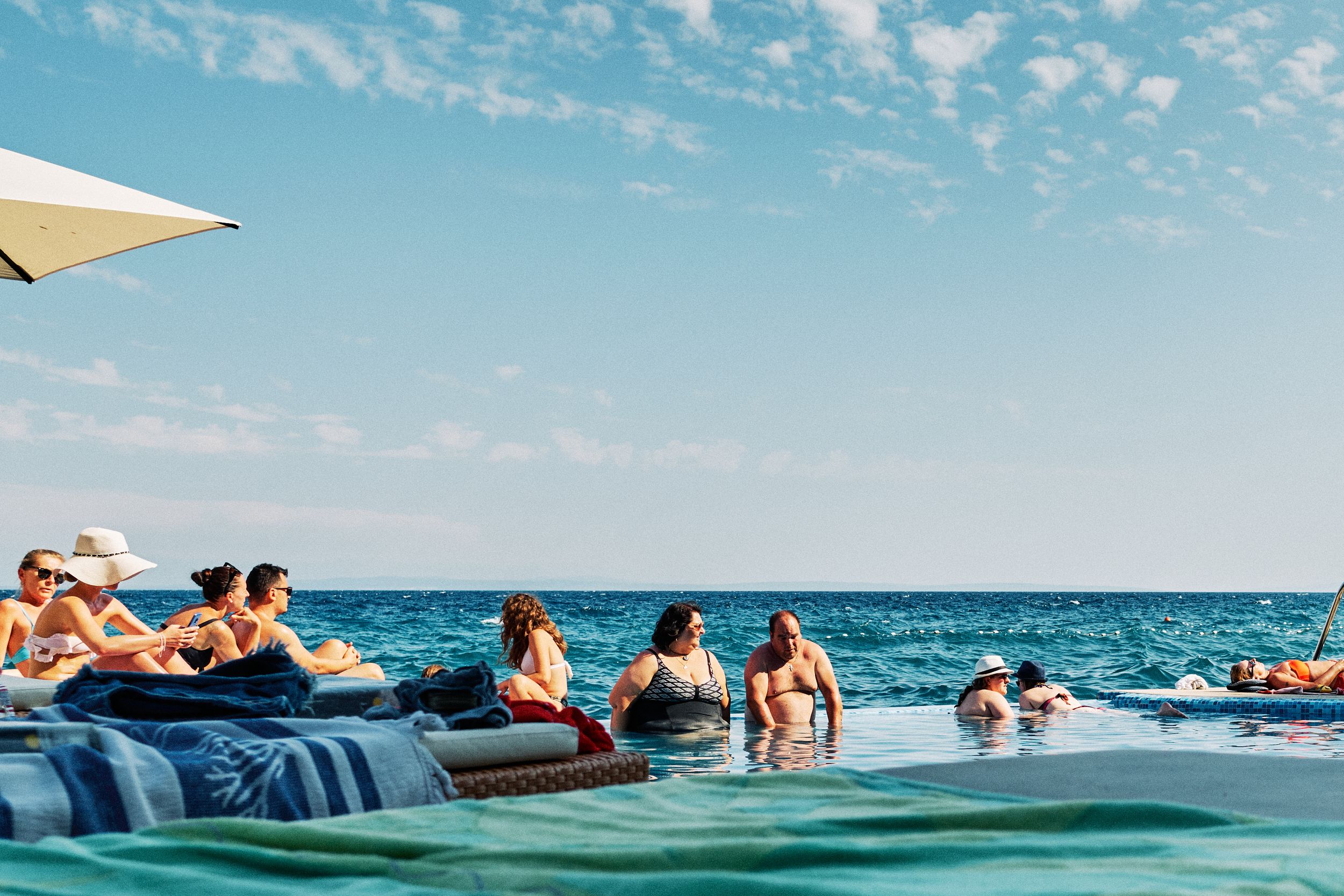 People relaxing at an infinity pool overlooking the blue ocean.