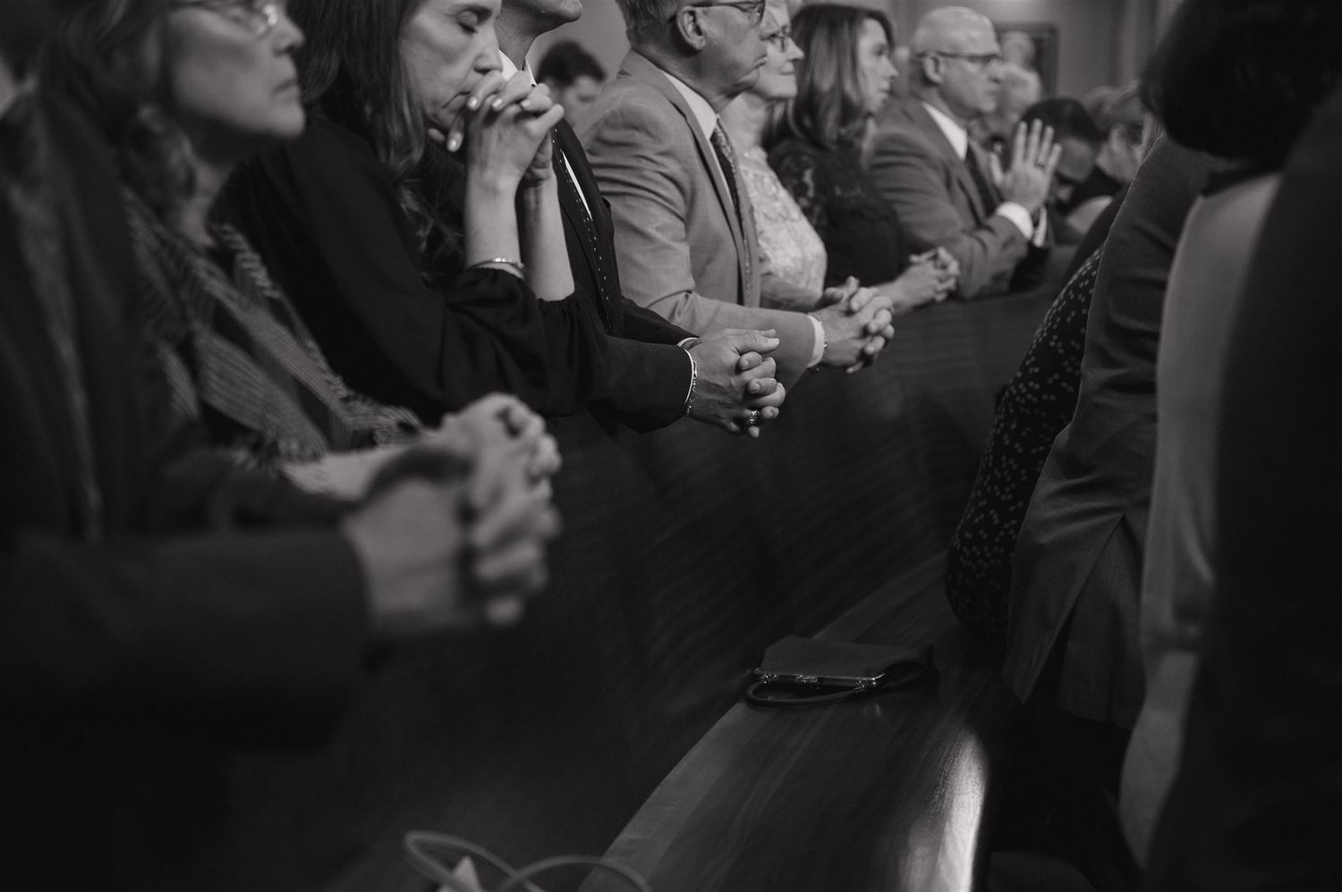 Black and white photo of wedding guests praying during ceremony in church pews.