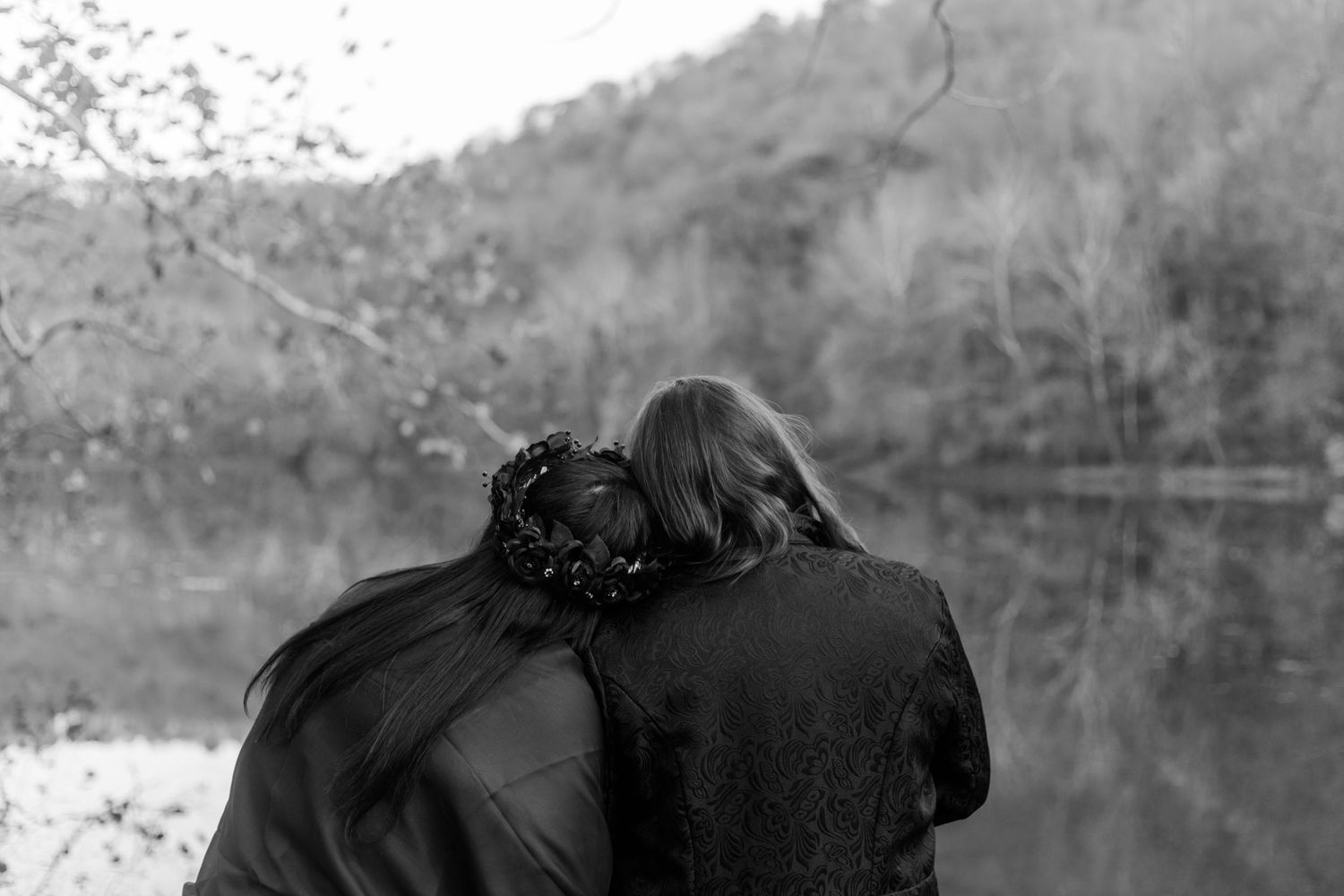 Dark silhouettes stand against a moody lake backdrop with mountains in the distance.