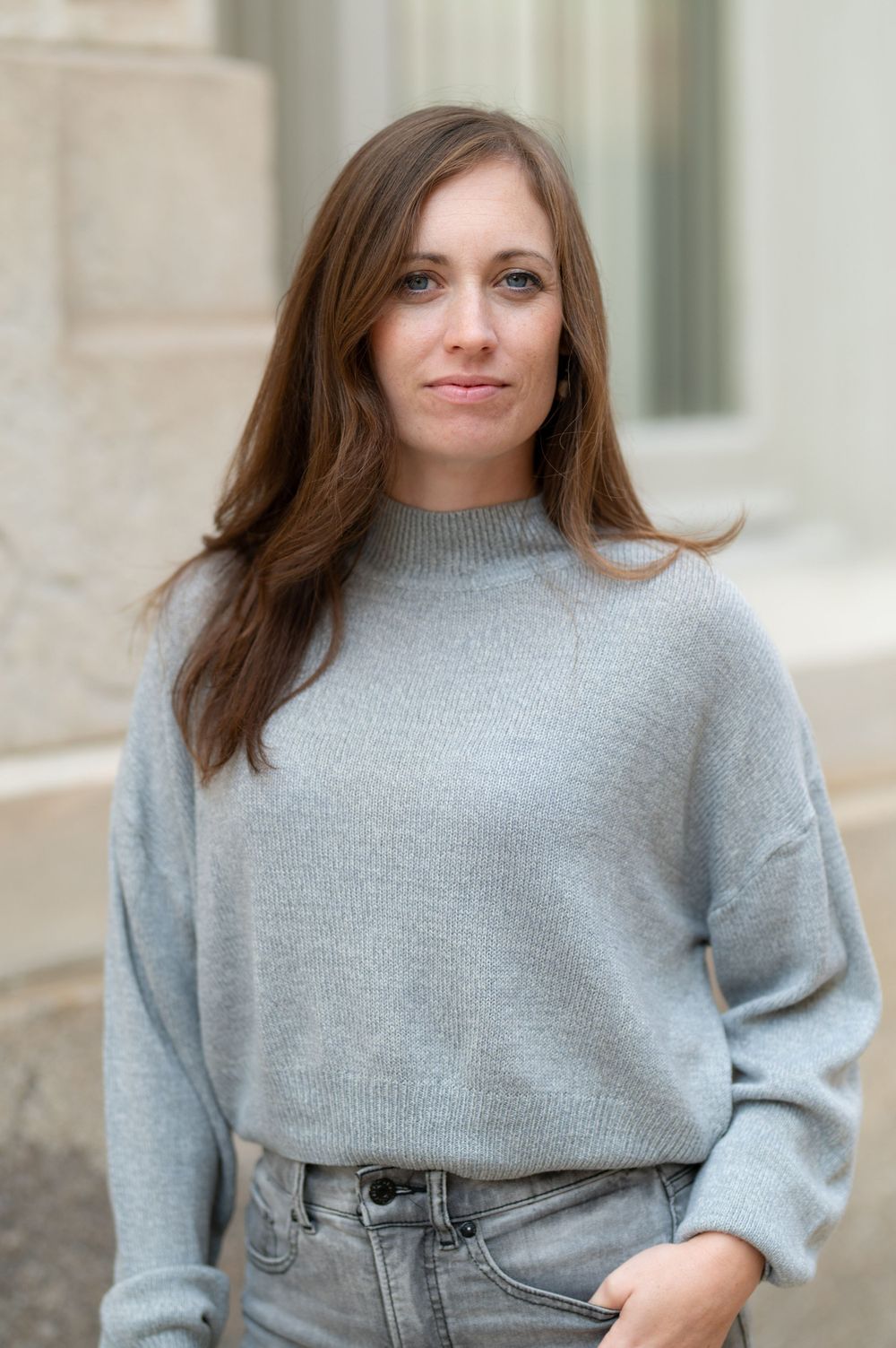 Casual portrait against stone columns wearing gray sweater and denim.