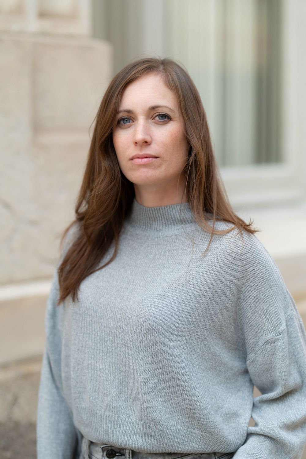 Close-up portrait in gray sweater against light stone architecture.
