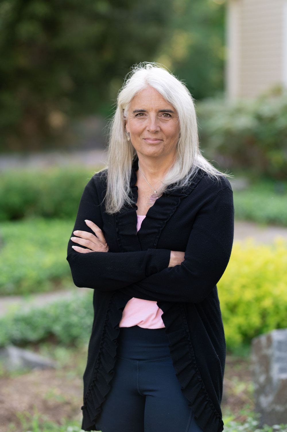 Professional portrait in an outdoor garden setting wearing a black cardigan over pink top.