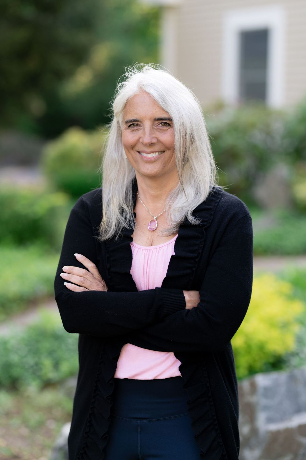 Casual outdoor portrait with silver hair wearing black cardigan and pink top against garden backdrop.