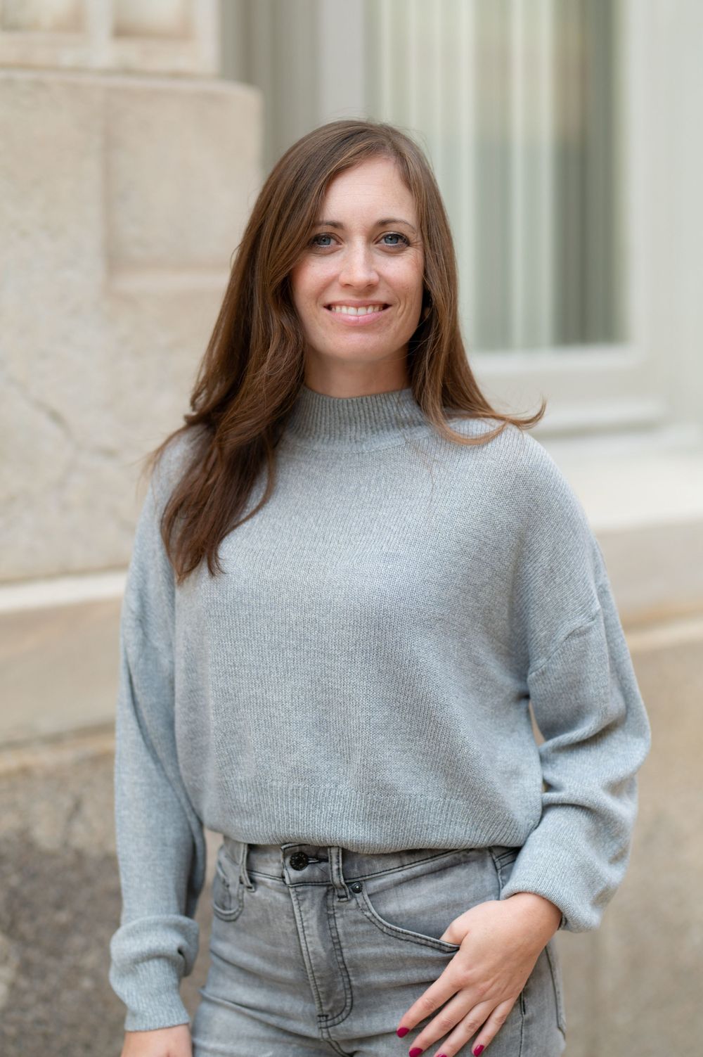 Relaxed portrait shot featuring gray sweater and jeans against architectural backdrop.