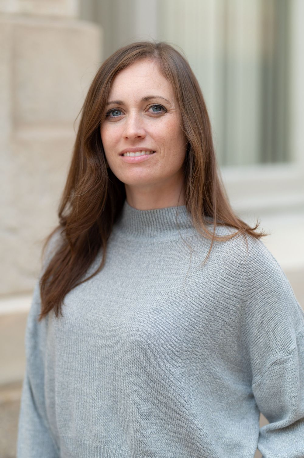 Portrait against stone building wearing comfortable gray knitwear.