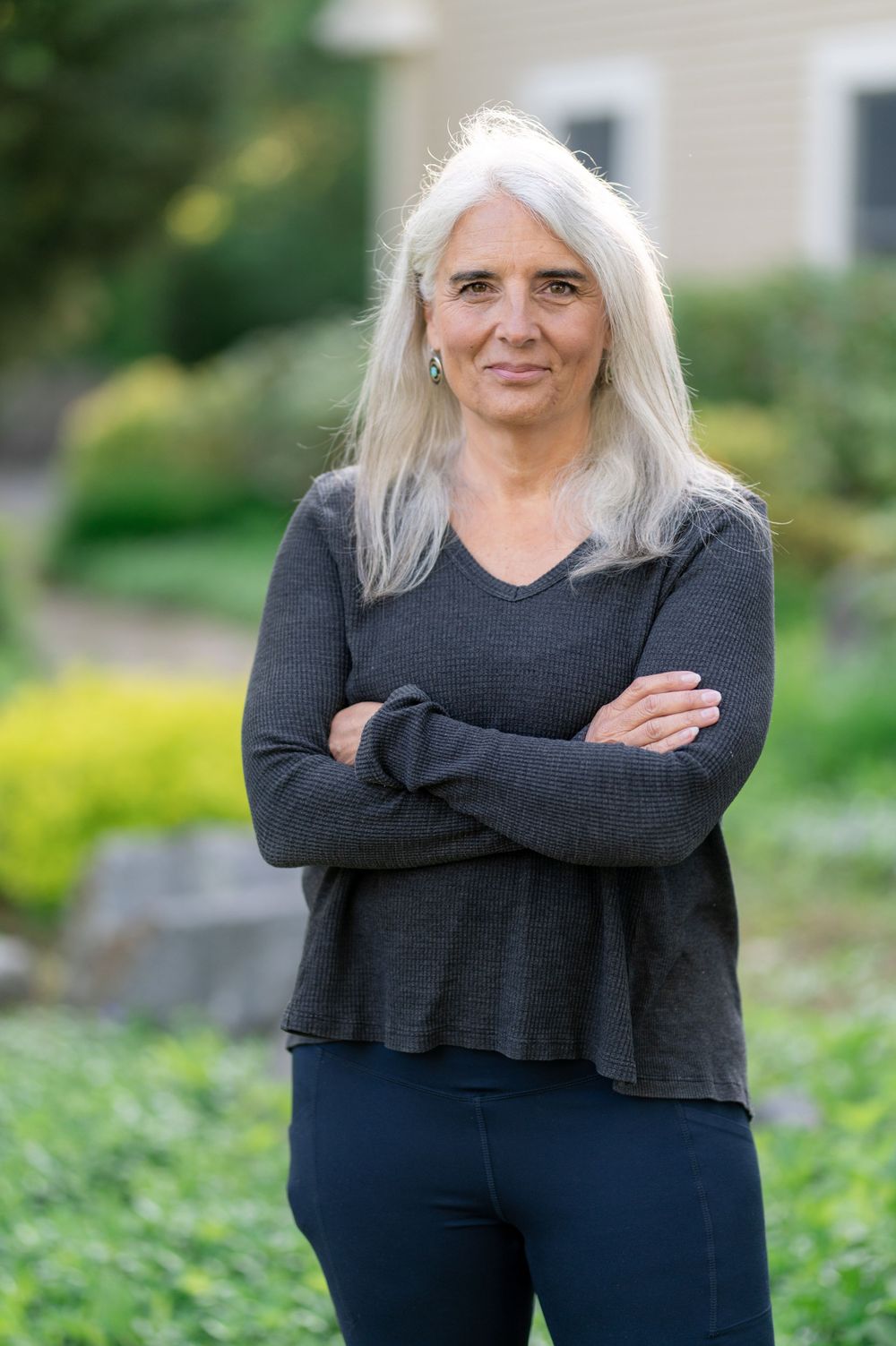 Professional portrait in dark v-neck sweater with garden scenery.