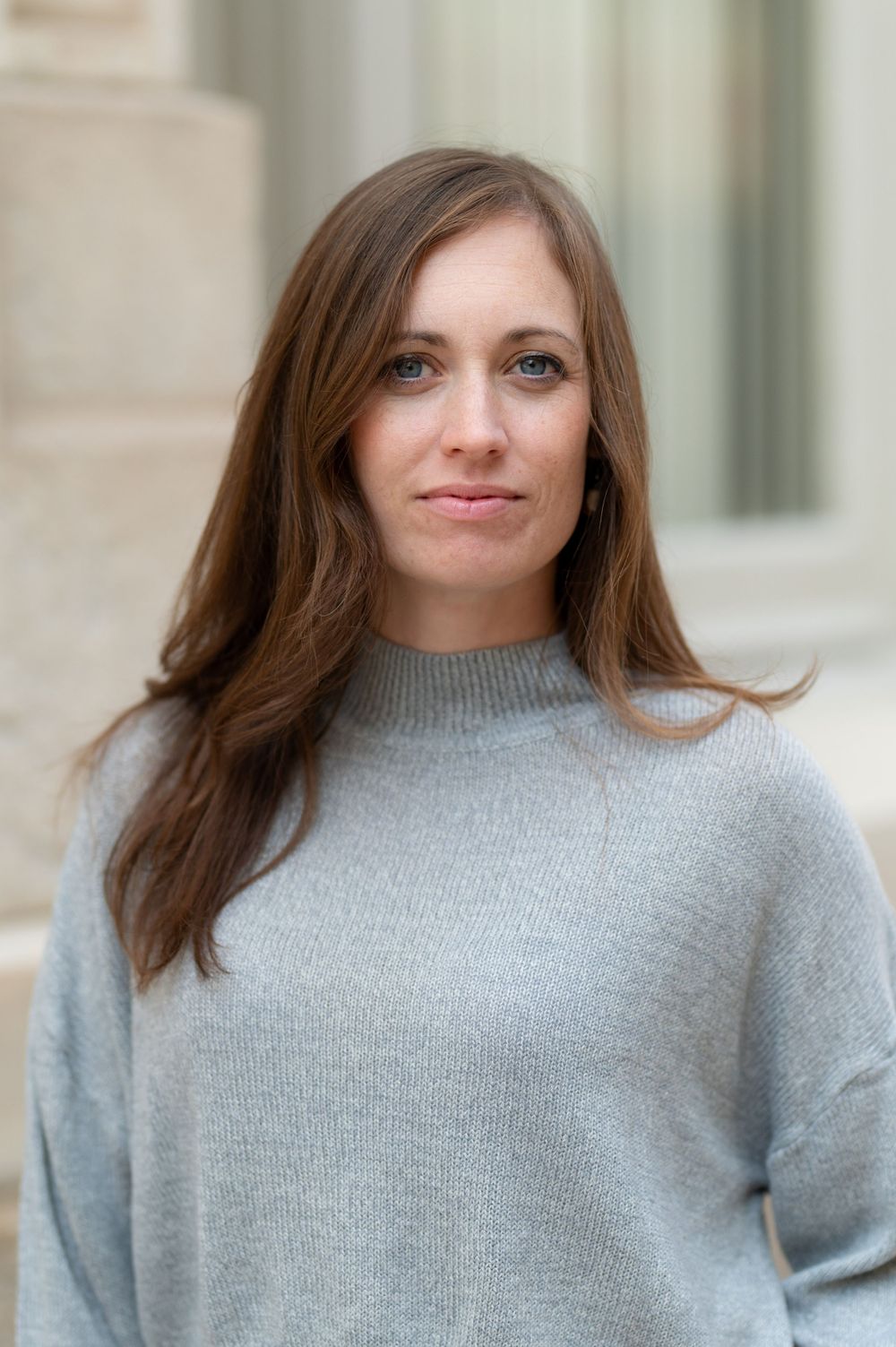 Portrait of someone in a cozy gray sweater against a light architectural background.