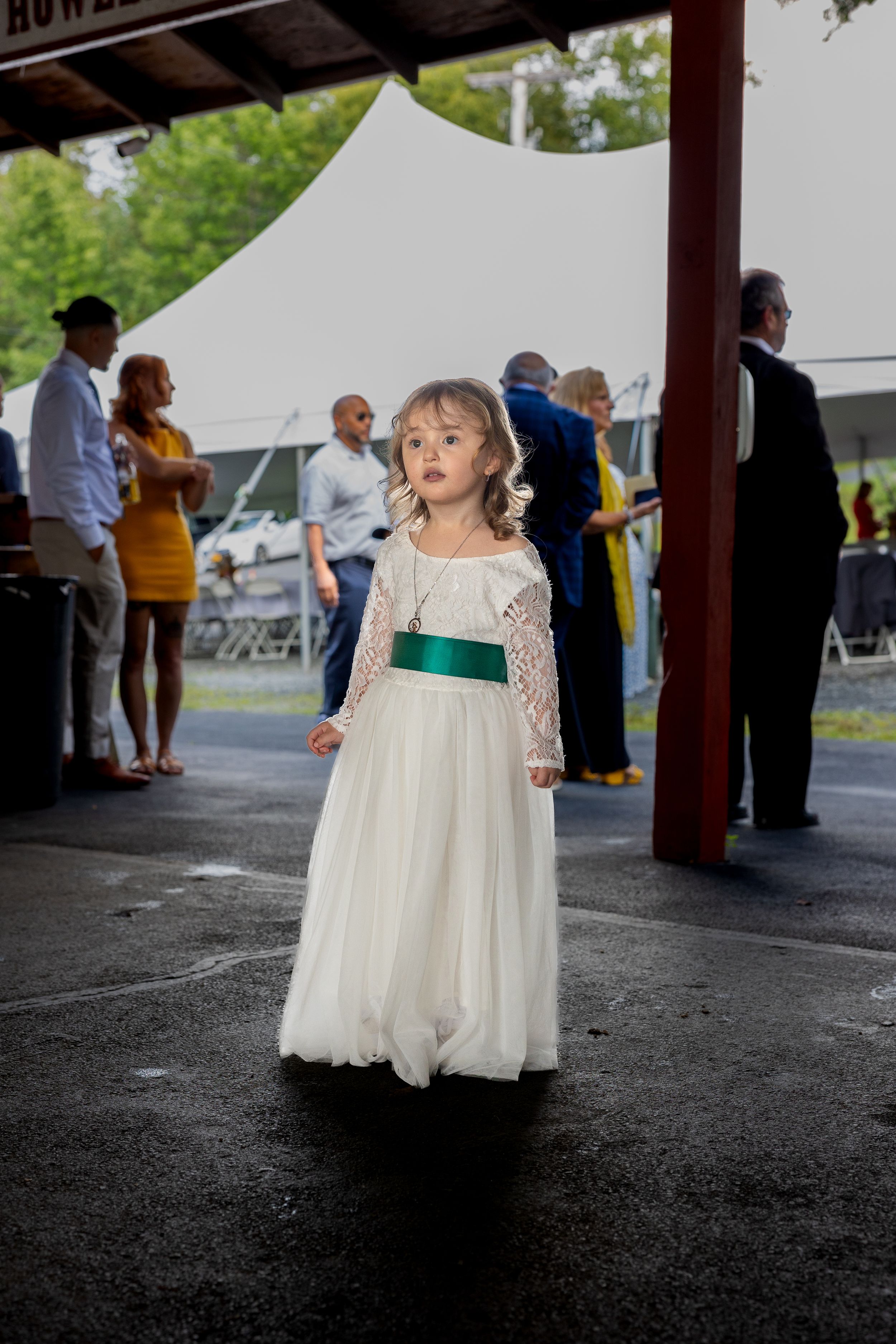 Young flower girl in white lace dress with green sash at wedding reception.