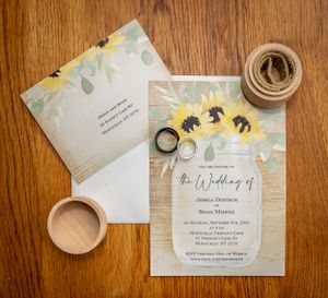 Sunflower-themed wedding invitation suite with mason jar design and rustic twine on wooden surface.