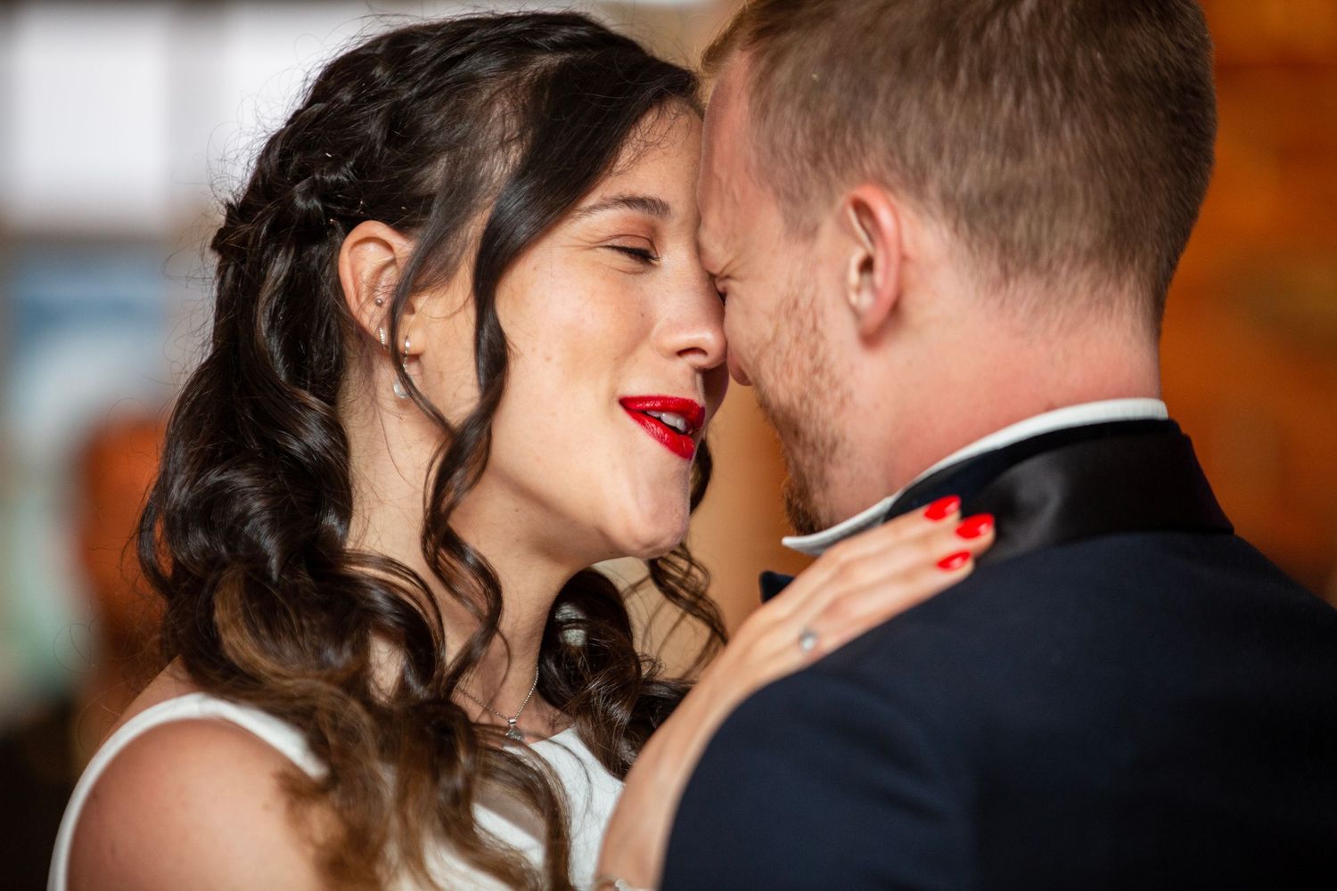 Romantic couple shares an intimate dance moment at a wedding reception with warm lighting and brick wall backdrop.