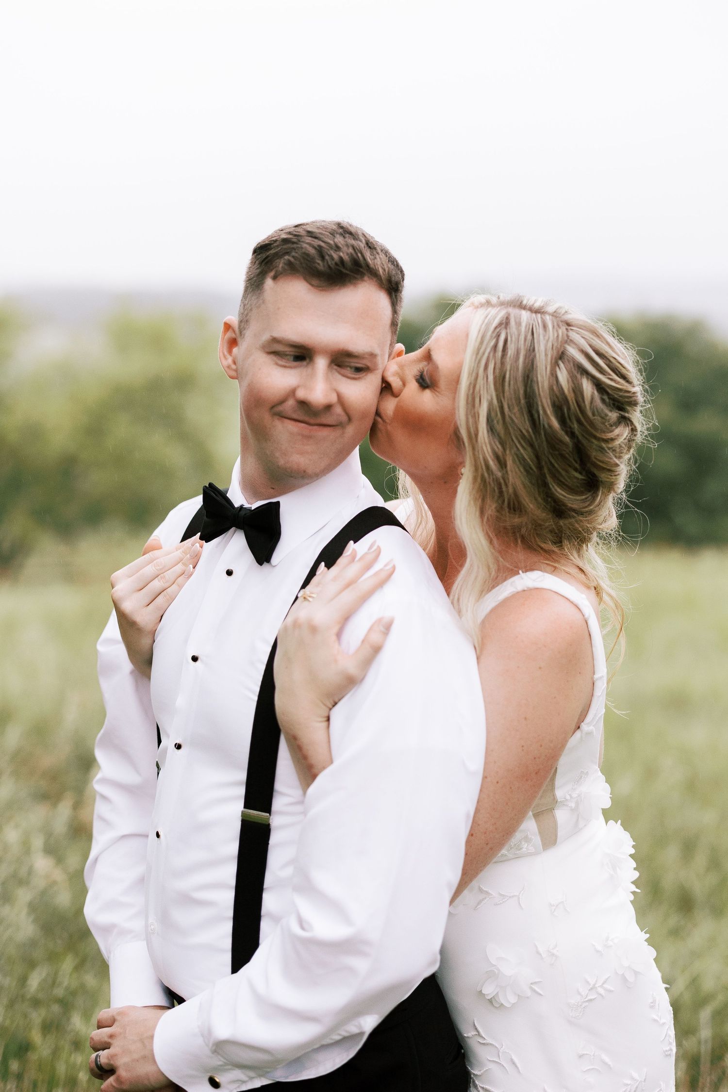 A romantic wedding moment captured outdoors with the bride kissing her groom in formal attire.