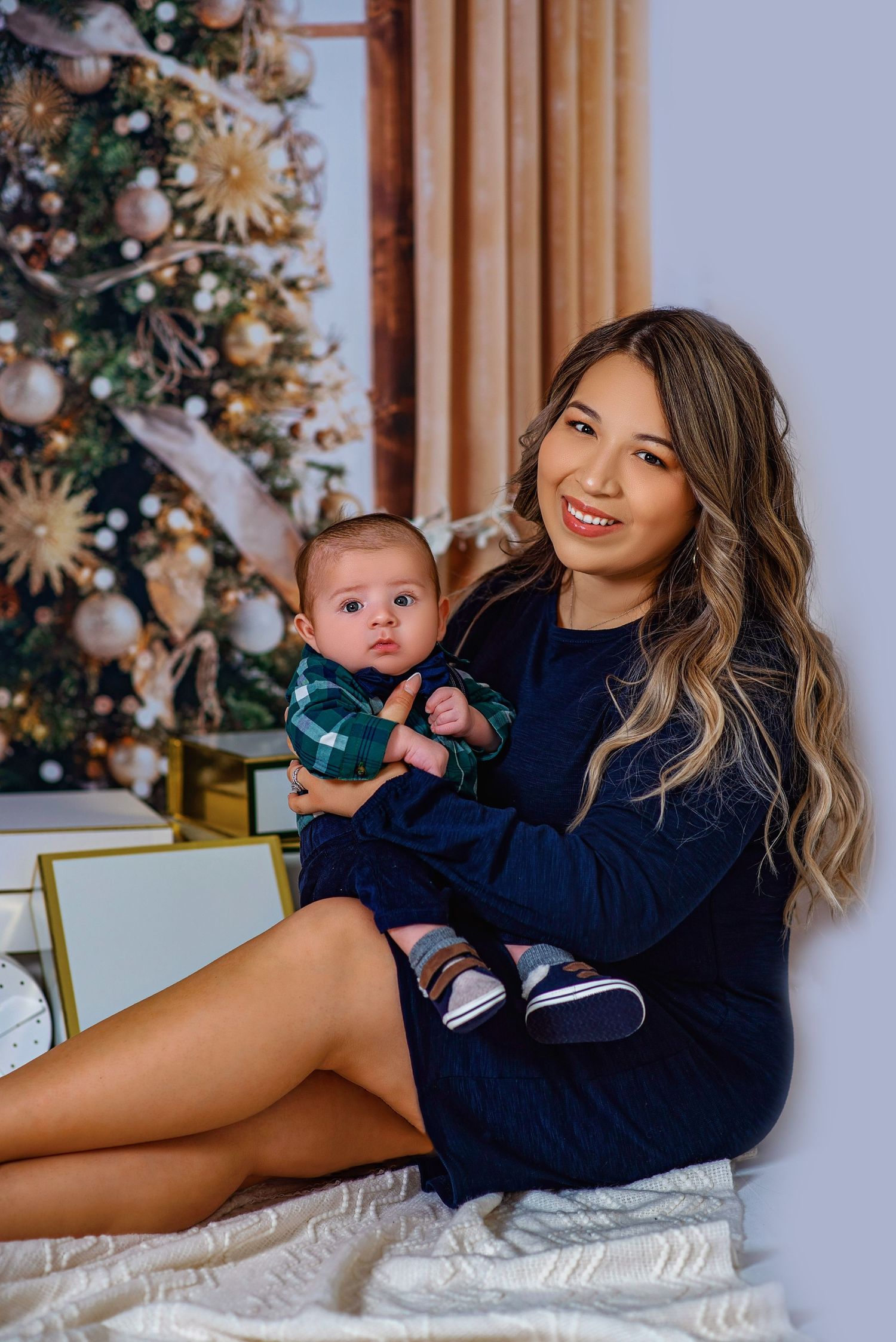 Cozy holiday photoshoot by Christmas tree in navy sweater.
