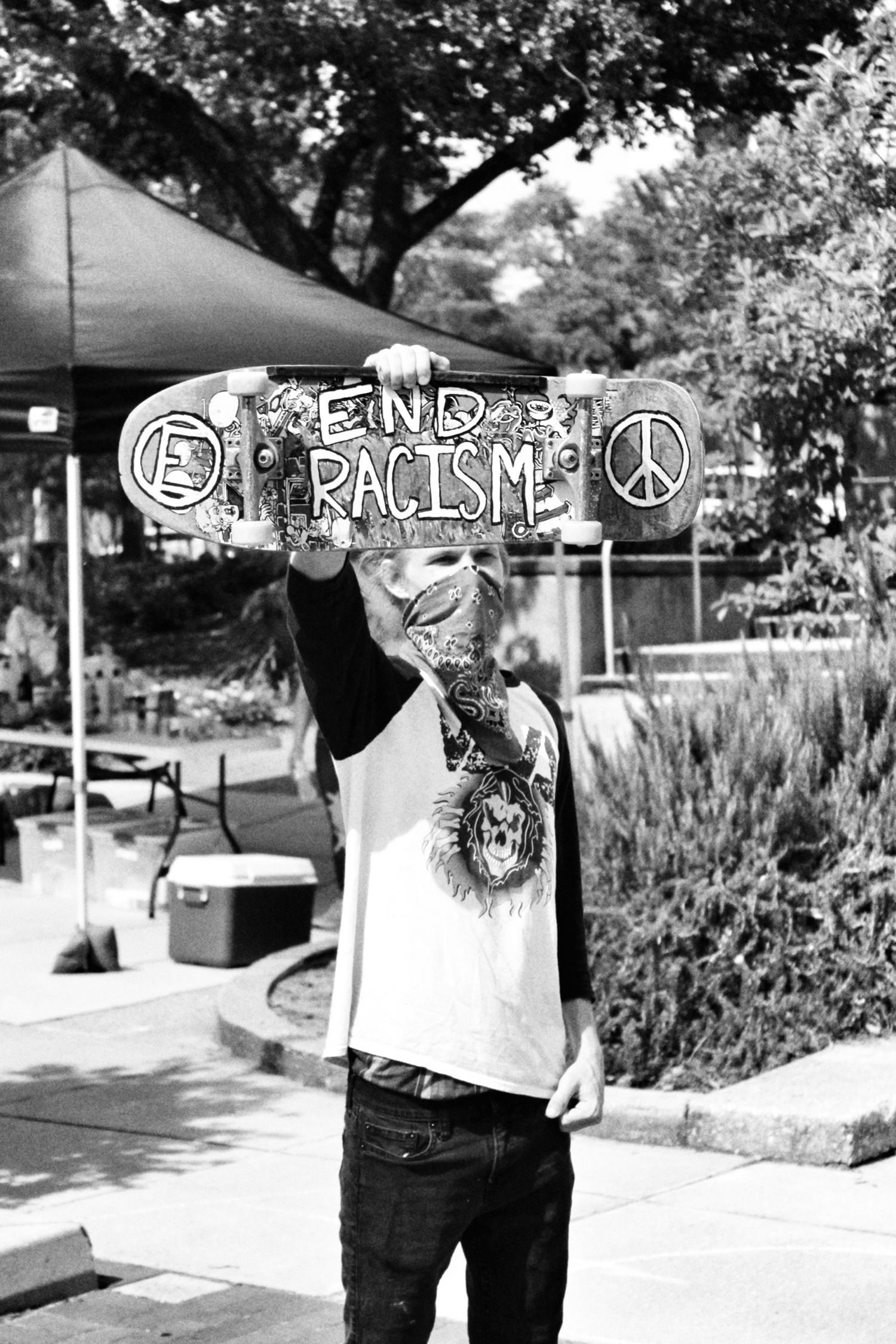 A black and white photo of someone holding a sign that says 'End Racism' with peace symbols outdoors.