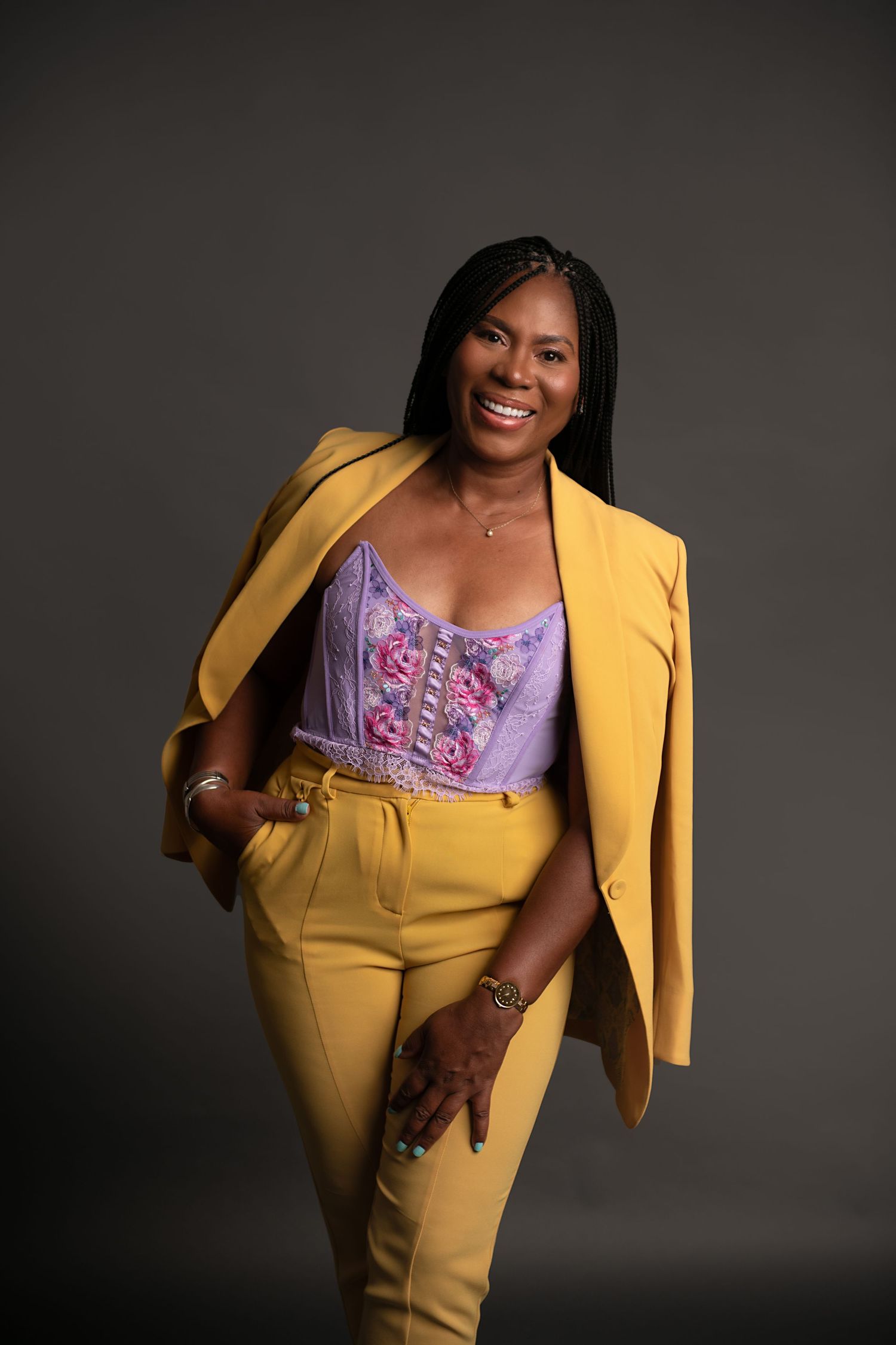Portrait of a woman in a yellow blazer and purple corset top against a dark background.