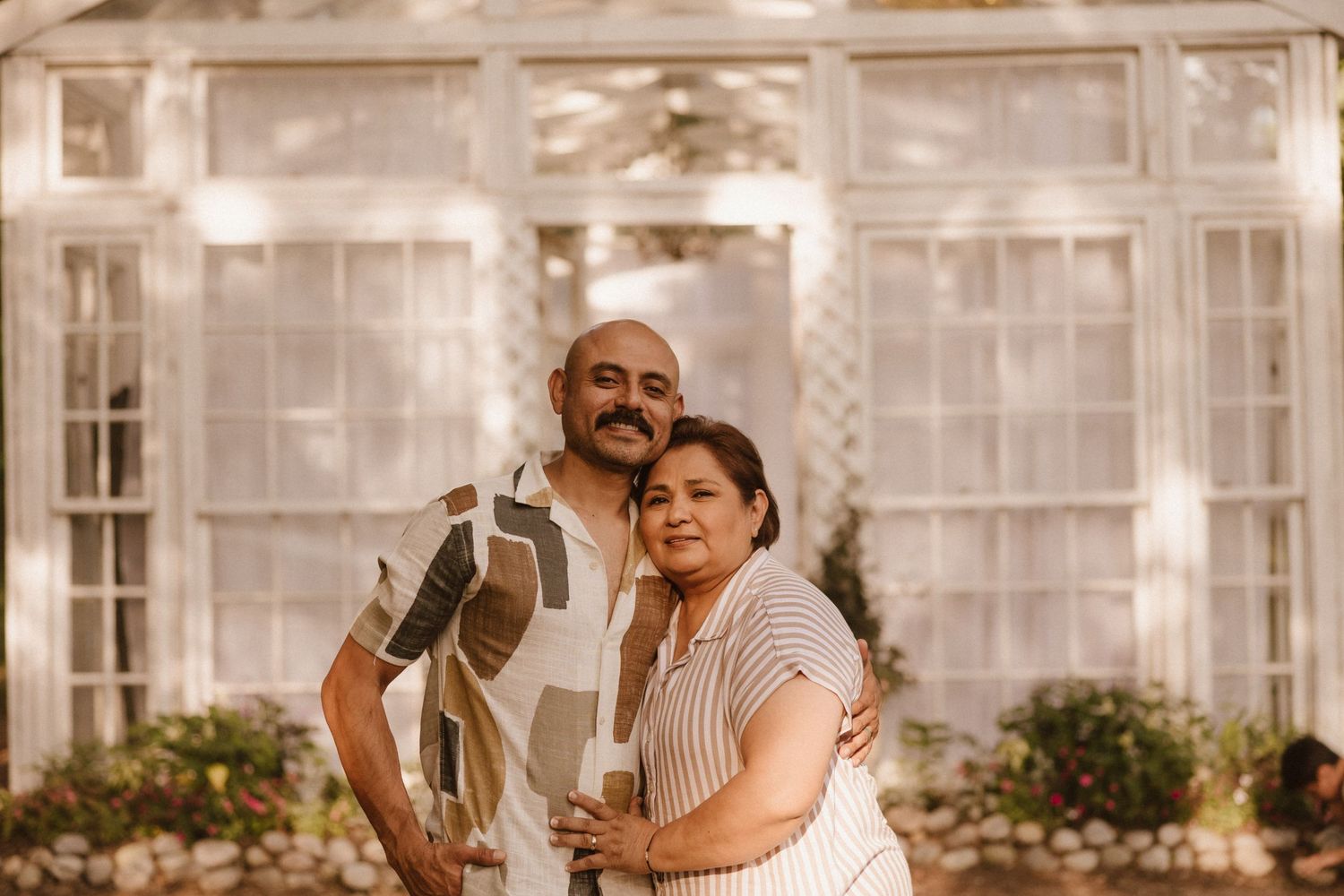 Warm-toned greenhouse portrait of couple in casual attire.