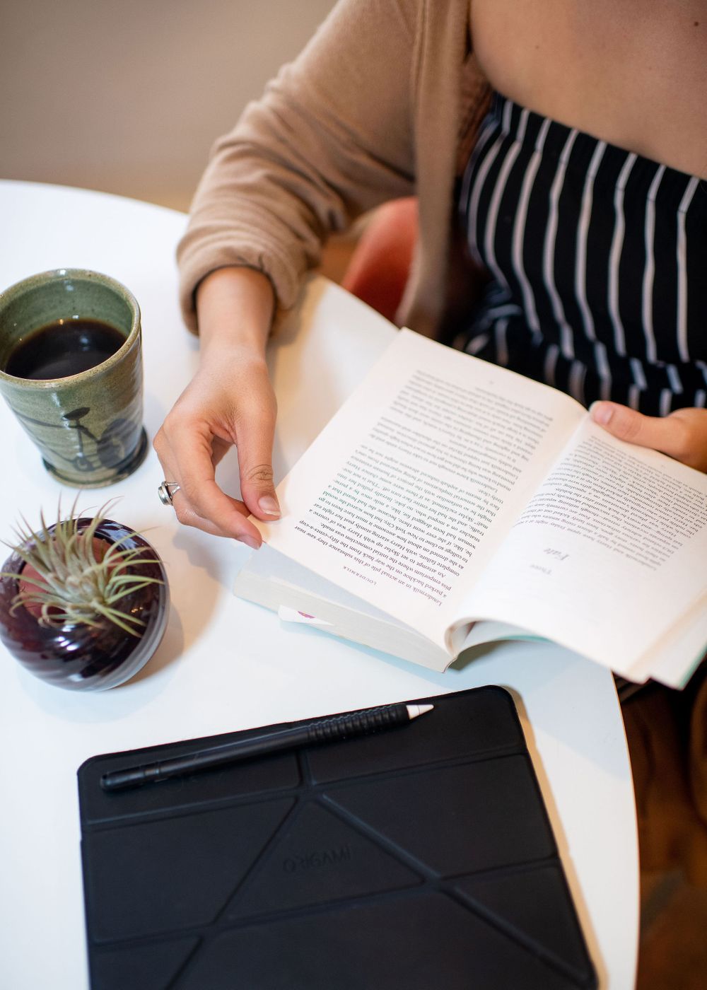 closeup photo of woman's hands reading book and drinking tea.