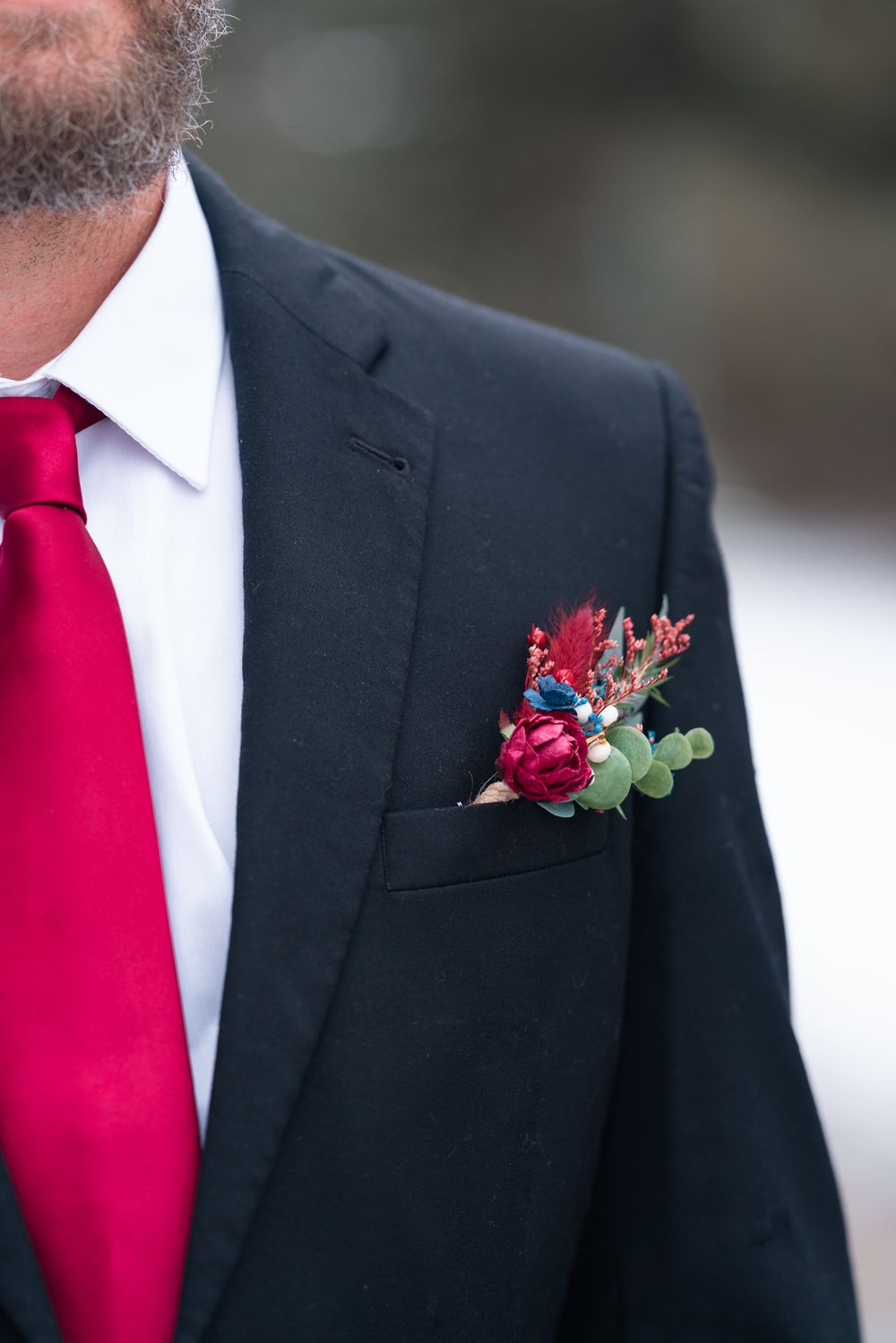 Close-up of red and burgundy floral boutonniere on black suit lapel with red tie.