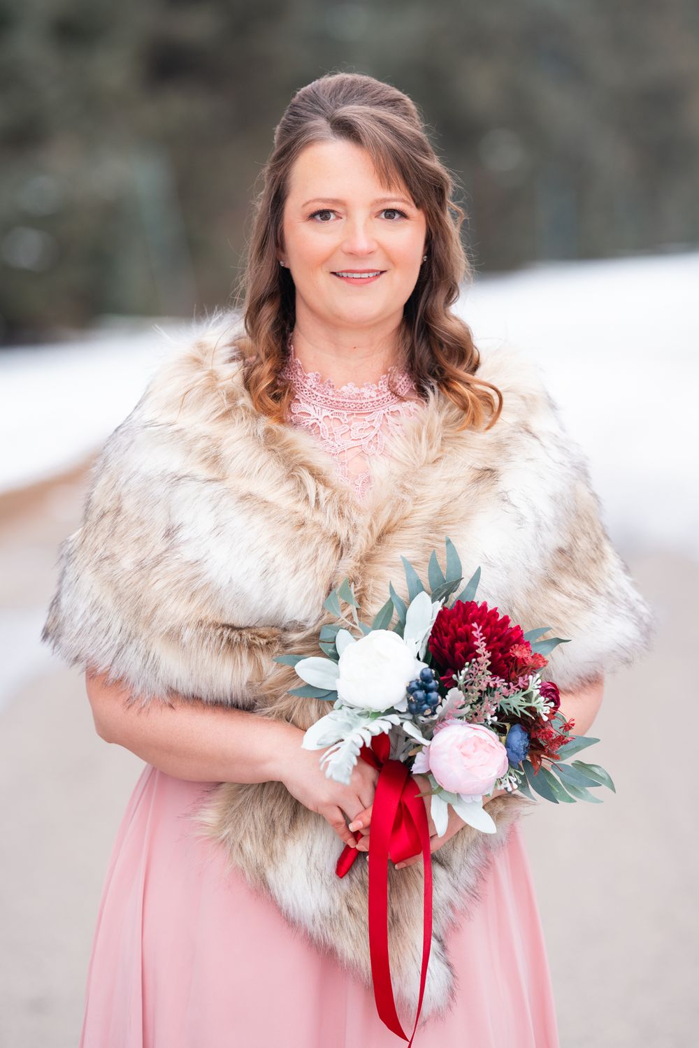 Bride in pink dress and fur shawl holds winter wedding bouquet.