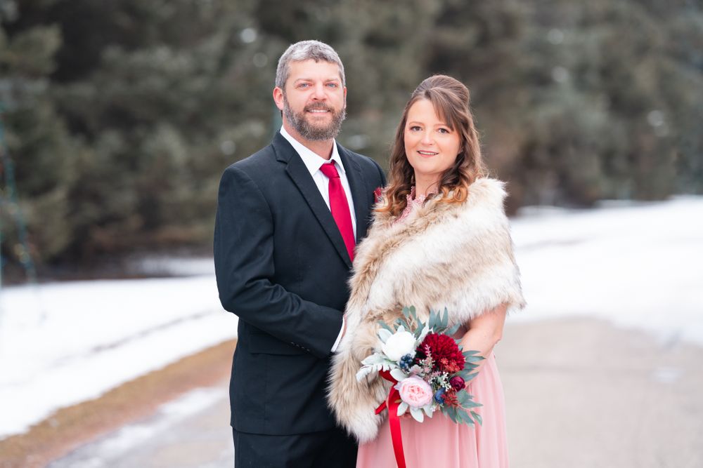 Winter wedding portrait of couple in formal attire against snowy evergreen backdrop.