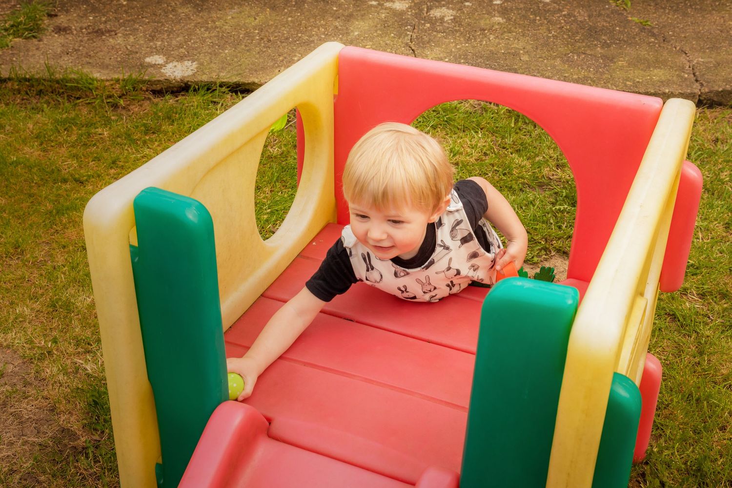 A child plays on a colorful plastic playground slide with red and green sides.