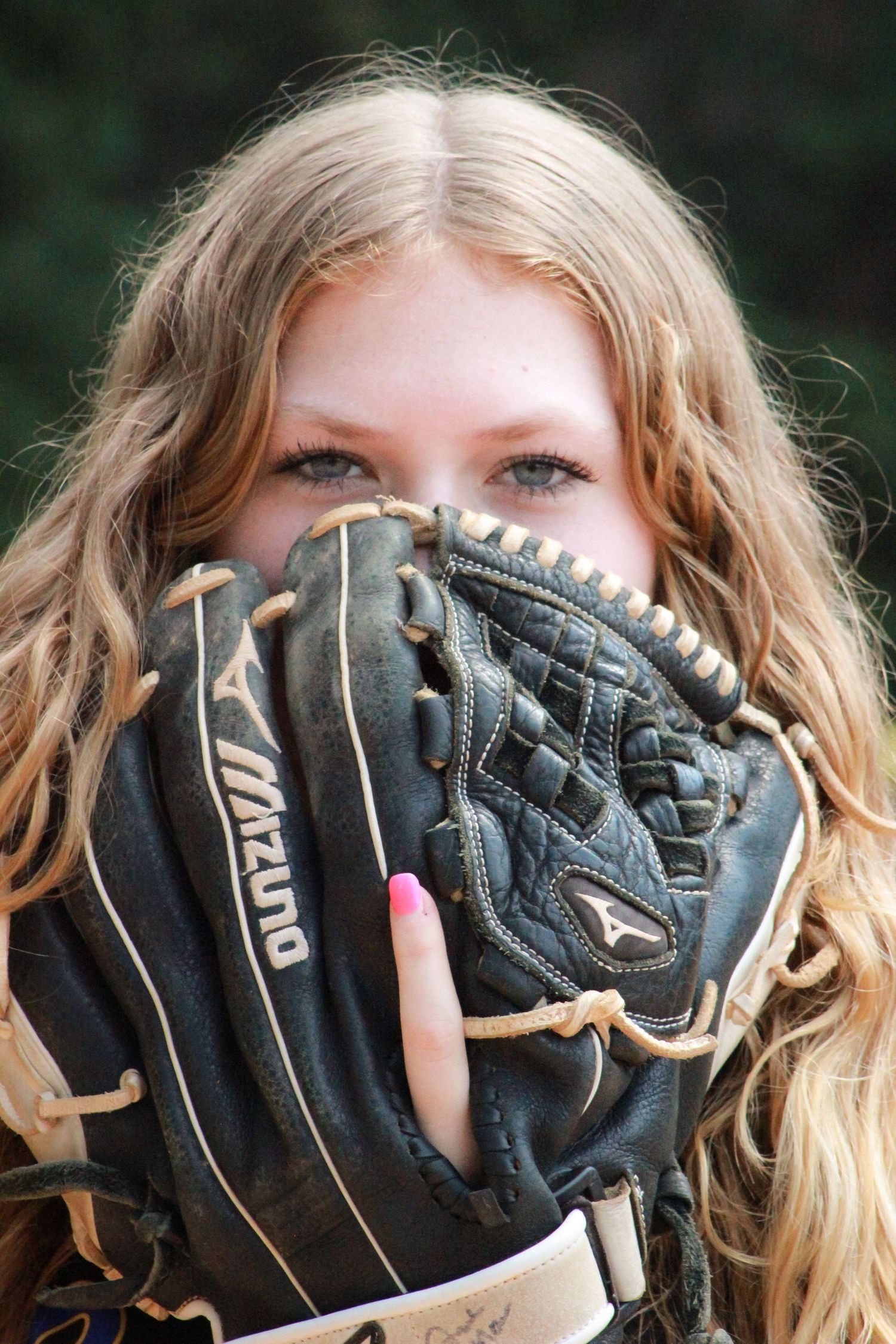 Sports portrait featuring black baseball glove held up in front of natural outdoor background.