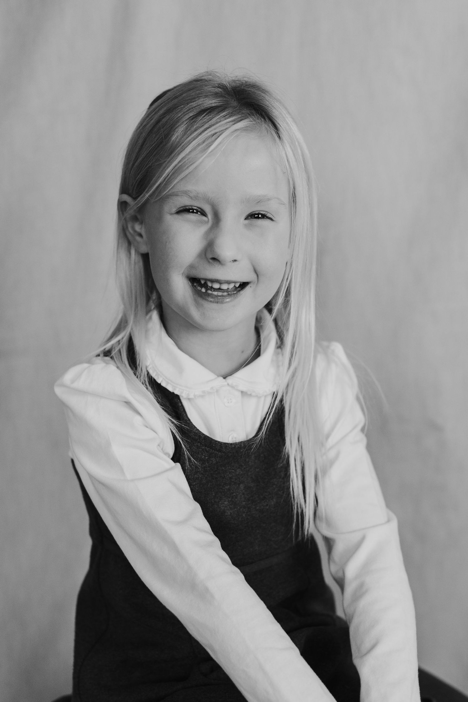 Student in white collar shirt and dark pinafore smiles brightly for school photo.