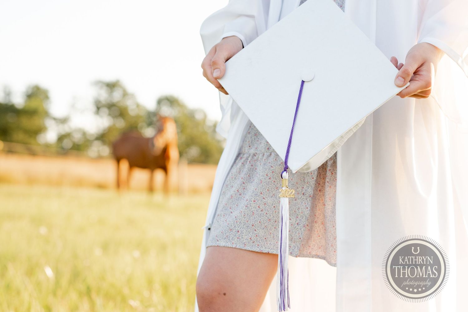 Close-up shot of white graduation cap and tassel against blurred pastoral background.