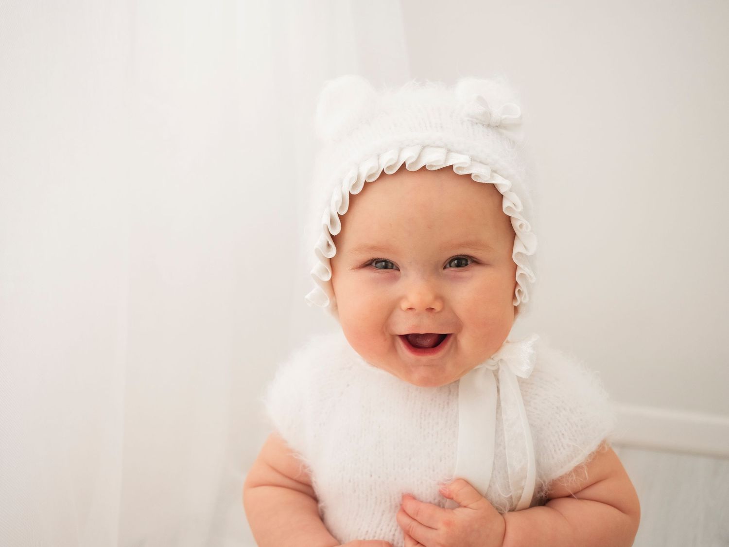 baby photo of girl in soft white outfit and bonnet smiling at camera