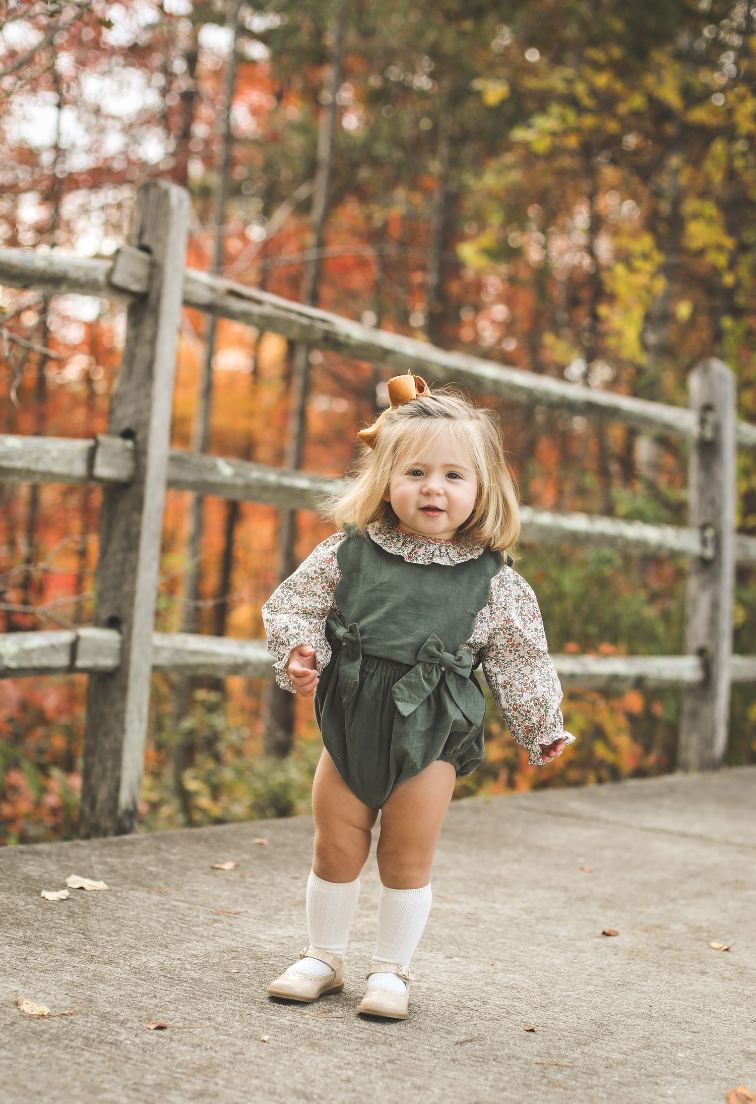 Child in green dress and floral top playing on wooden walkway during autumn.