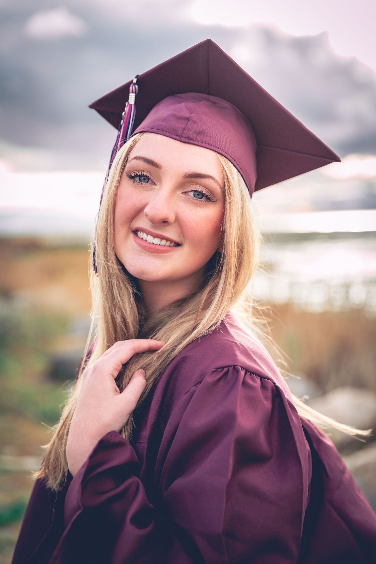 Young woman in graduation cap and gown smiling outdoors, captured in by Dillon Workman Photography LLC a senior portrait