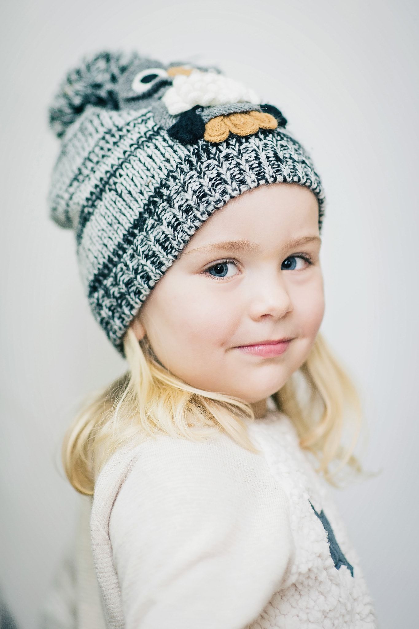 Child wearing knit pom pom beanie against light background.