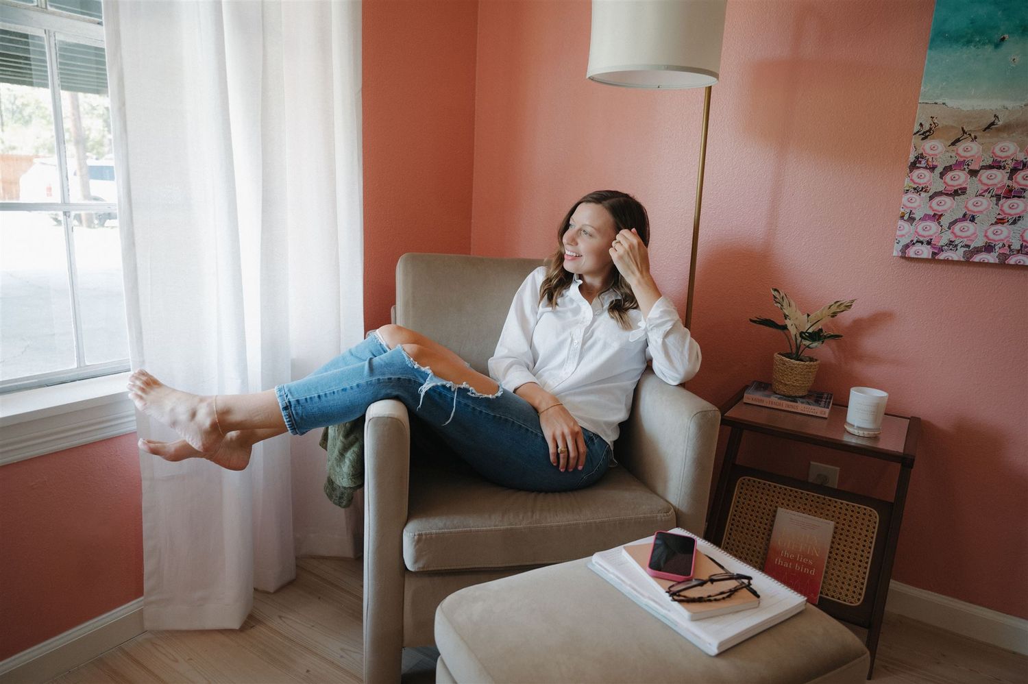 Someone relaxes in a cozy armchair with a pink accent wall and window in the background.