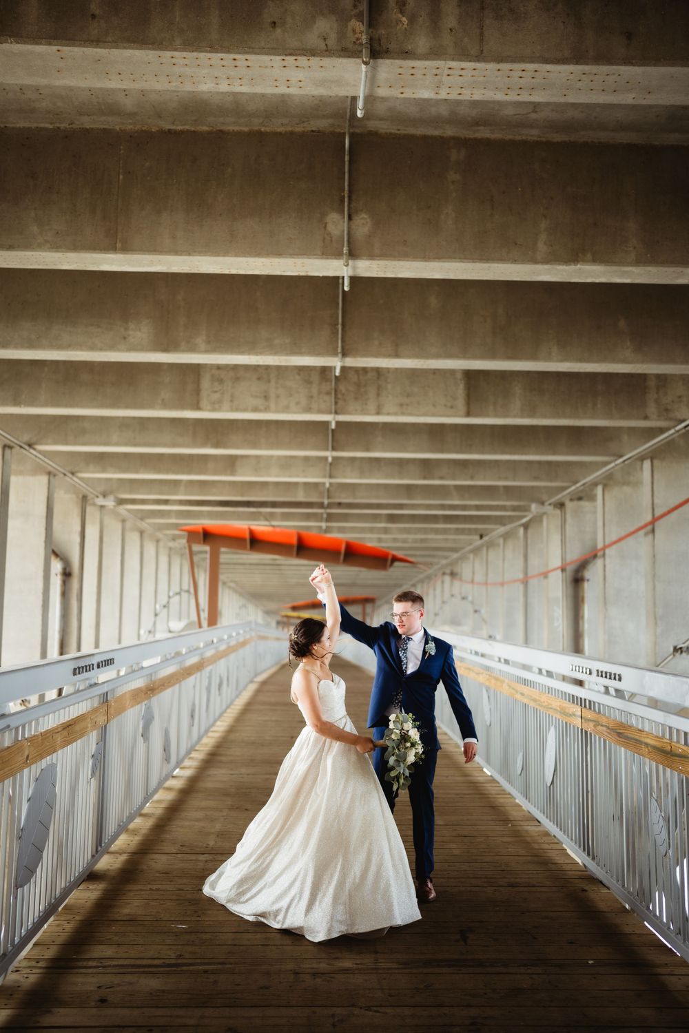 Newlyweds dancing in long white corridor with orange kayak mounted on wall.