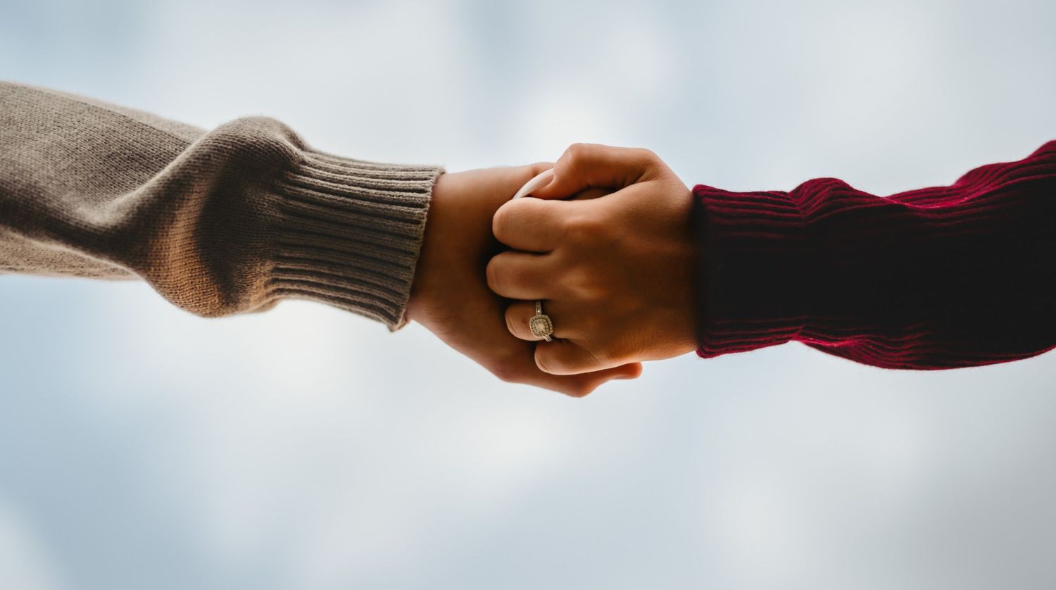 Two hands clasped together in a loving hold against a soft blurred background.