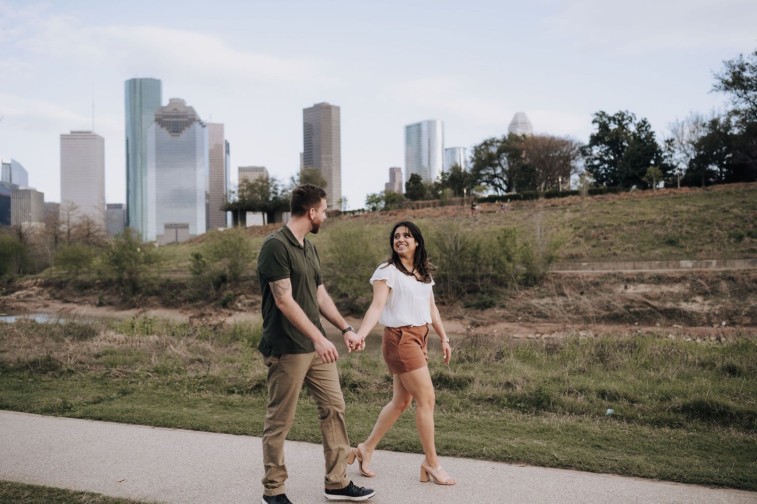 A couple walks hand in hand with Houston city skyline in the background.
