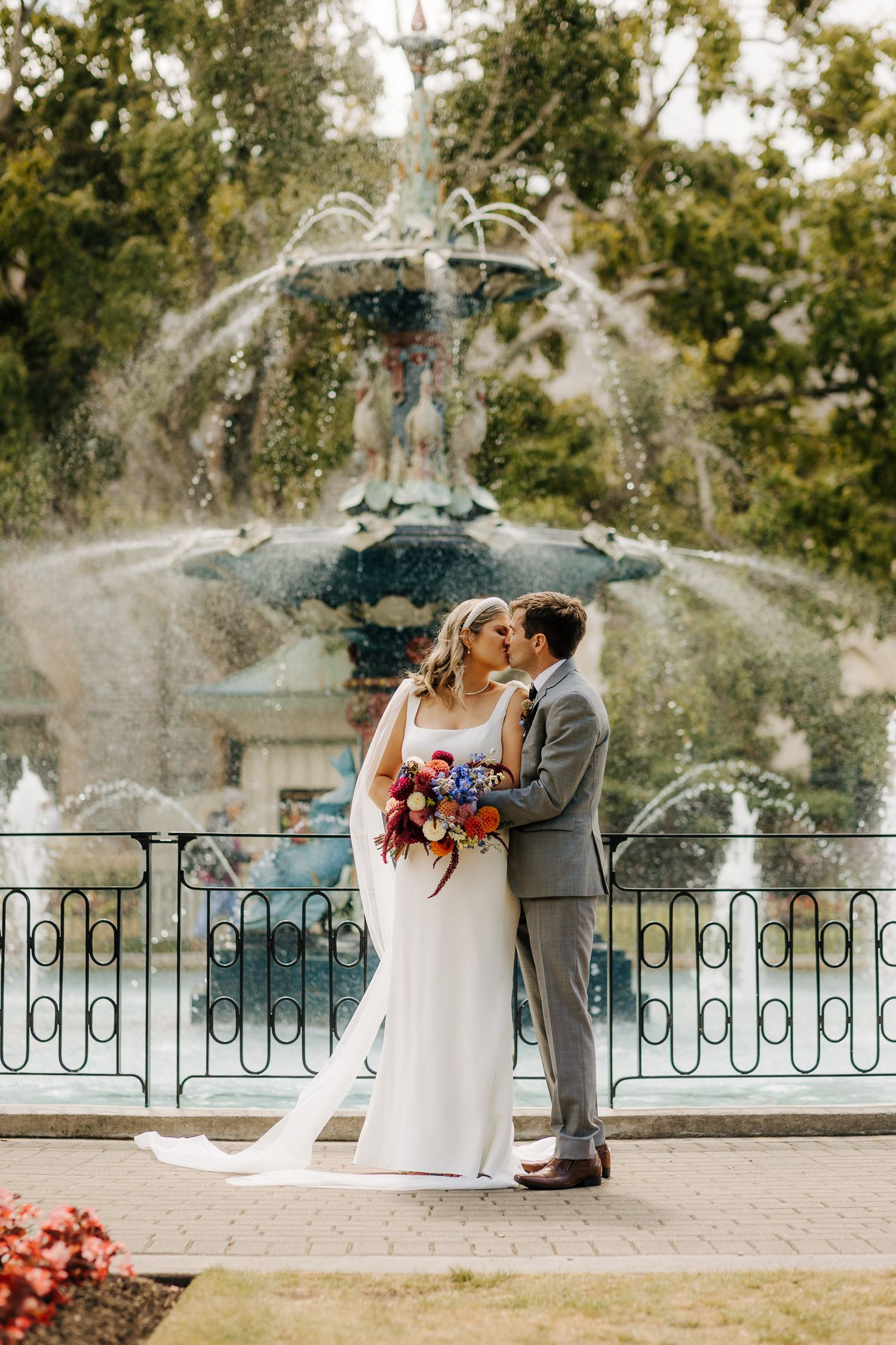 Groom kissing bride in front of the Peacock Fountain in Christchurch Botanic Gardens New Zealand